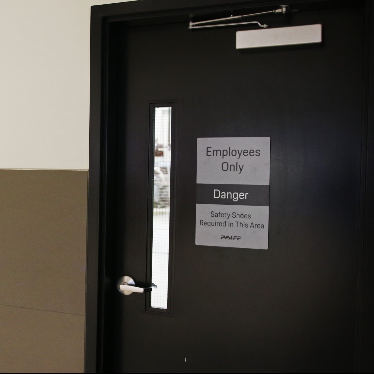Safety signage on a black door indicating "Employees Only," "Danger," and "Safety Shoes Required In This Area," featuring PFAFF branding, relevant to compliance with Ontario Building Code for the Porsche Centre Markham project.
