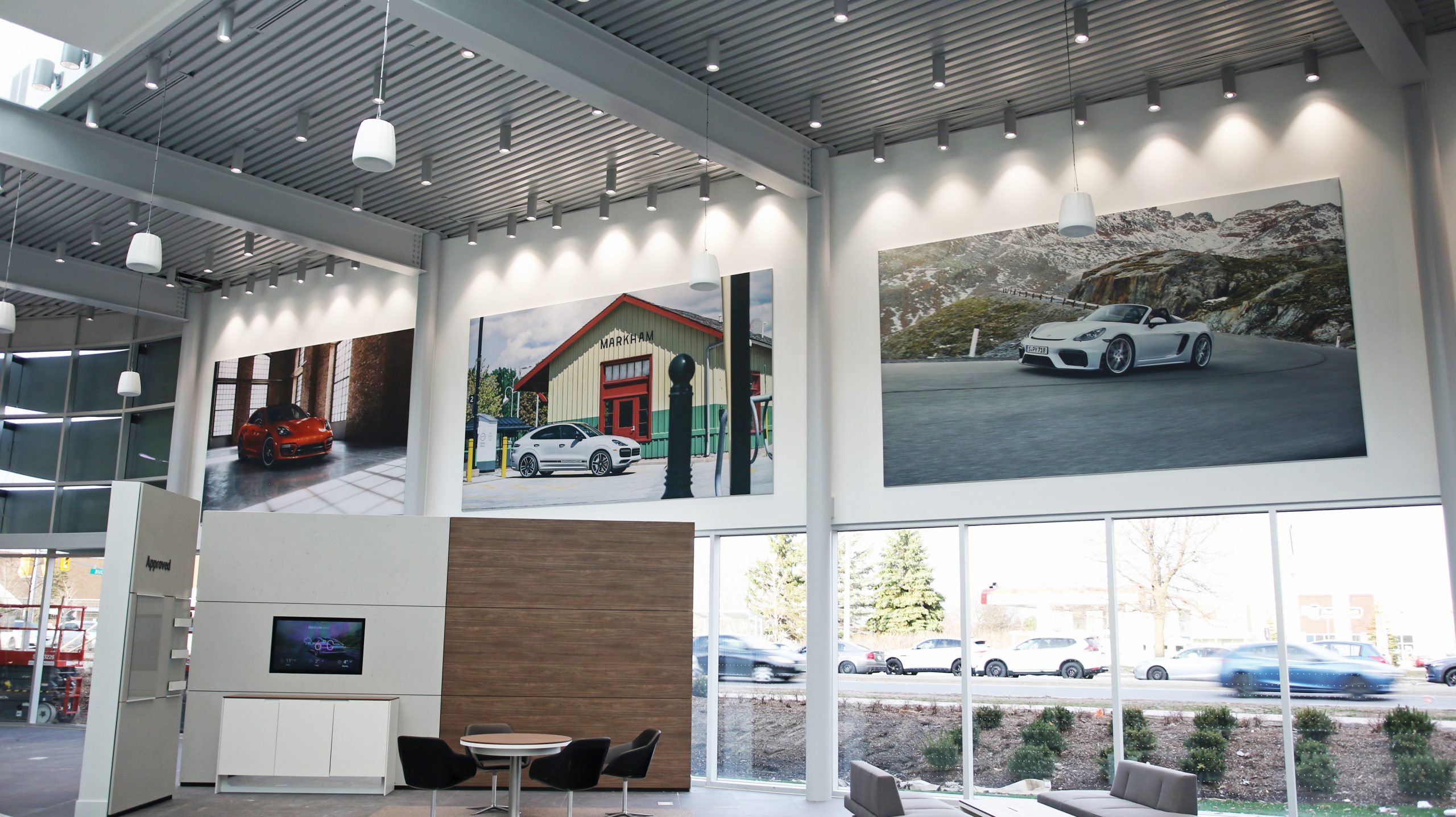 Showroom interior at Porsche Centre Markham featuring large fabric frames of Porsche vehicles, enhancing the customer experience with aspirational imagery above the main windows.