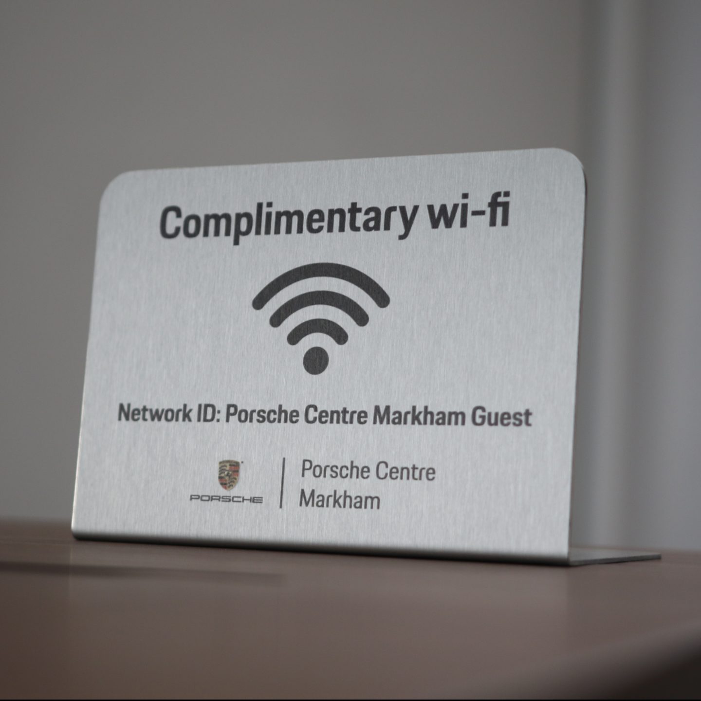 Metal Wi-Fi placard displaying "Complimentary Wi-Fi" and "Network ID: Porsche Centre Markham Guest," featuring Porsche branding, relevant for dealership customer experience.